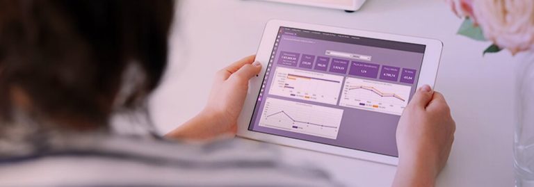 Pessoa usando um tablet com um dashboard interativo na tela, exibindo gráficos e métricas em tons de roxo.